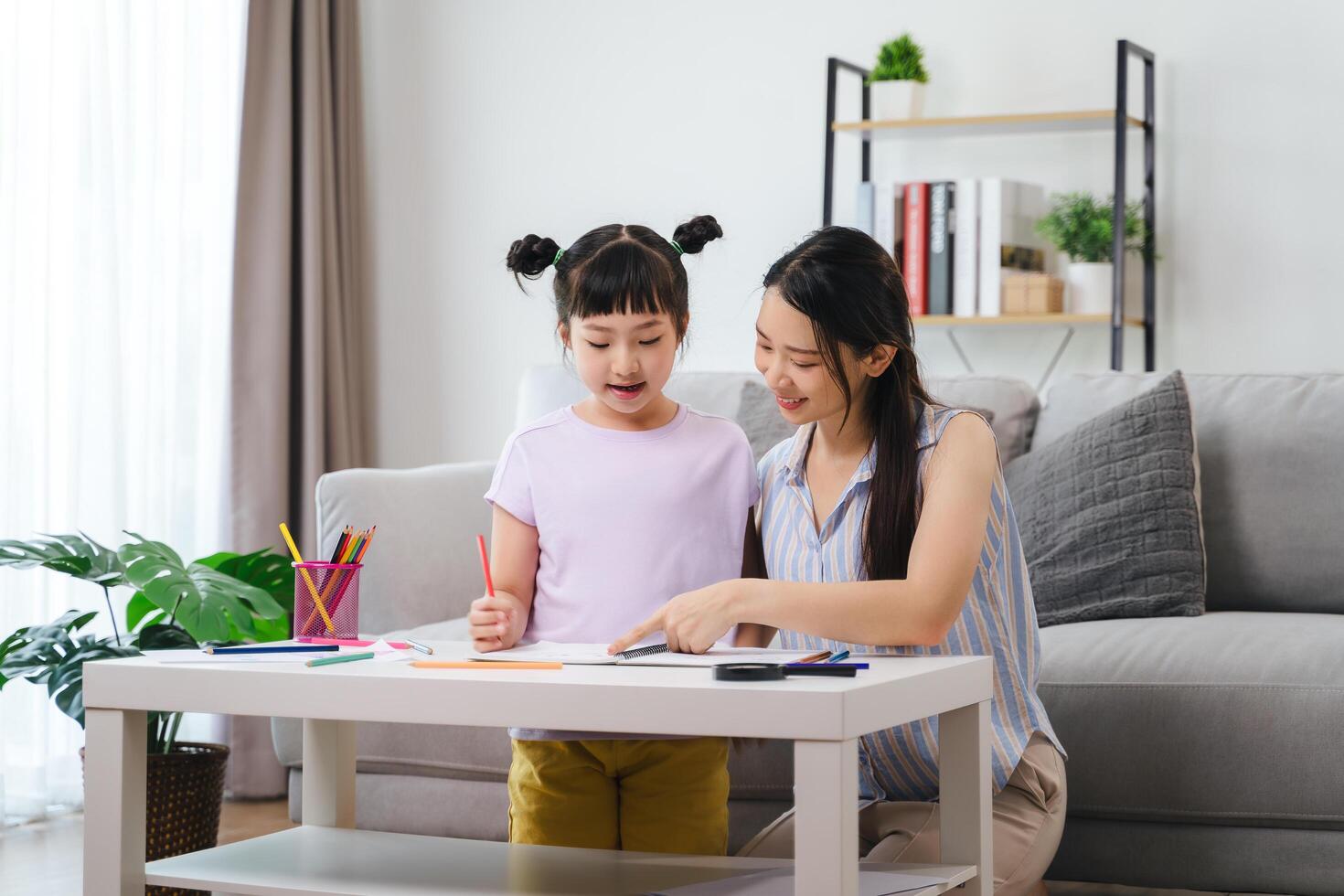 A woman and a child are sitting at a table with a book and a pencil photo