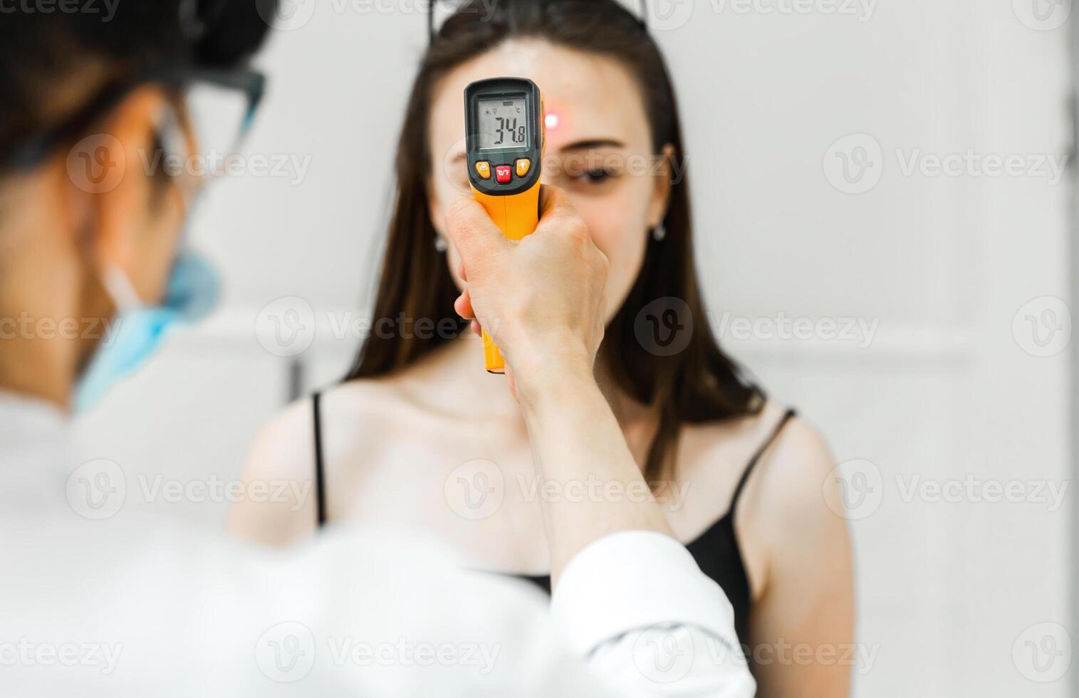 Healthcare Worker Checking Woman's Temperature with Infrared Thermometer photo