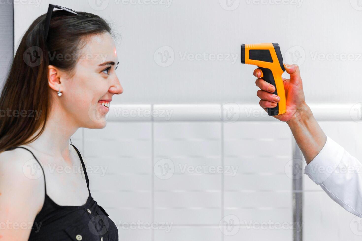 Smiling Woman Undergoing Temperature Check with Infrared Thermometer photo