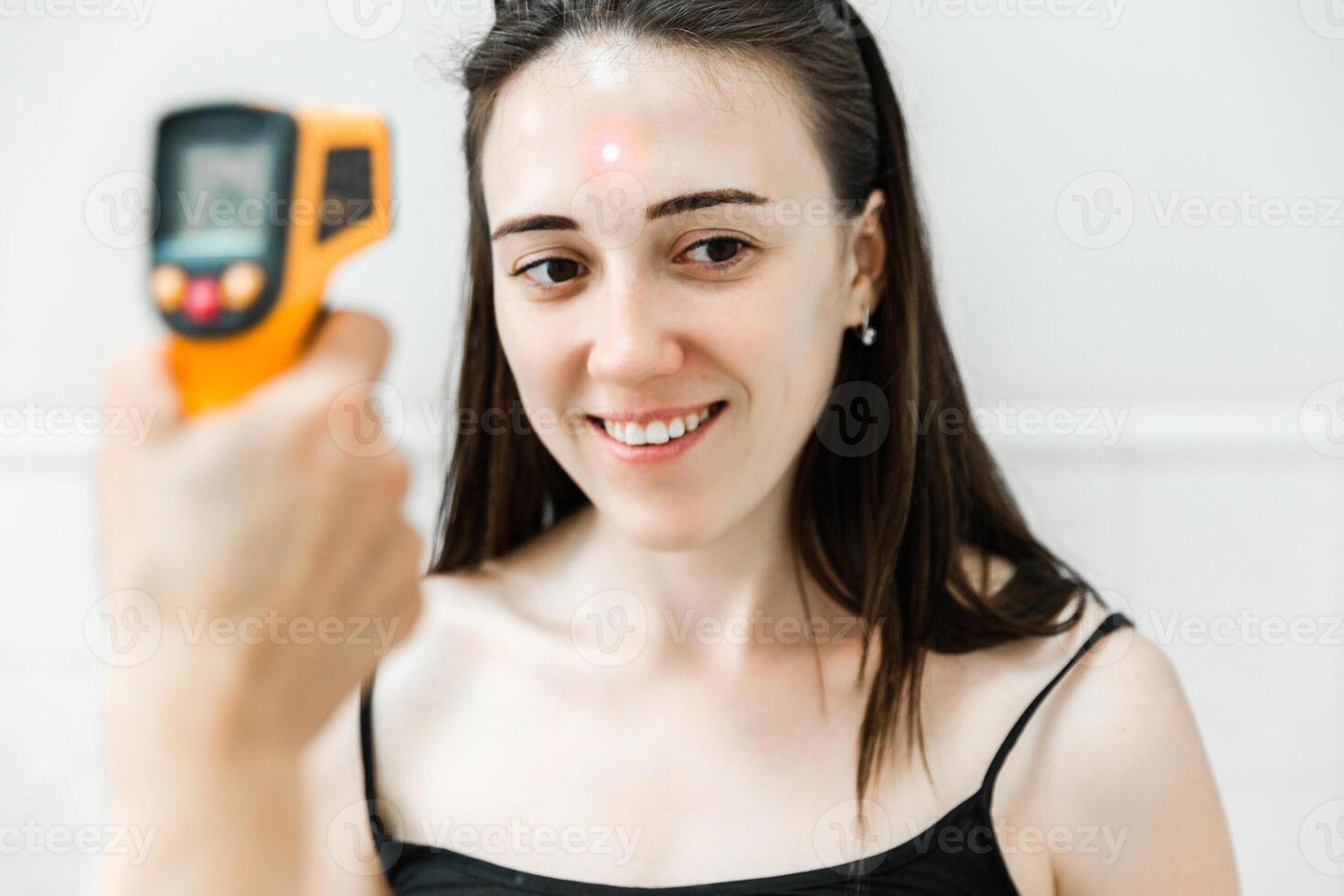 Smiling Woman Having Her Forehead Temperature Checked with Infrared Thermometer photo