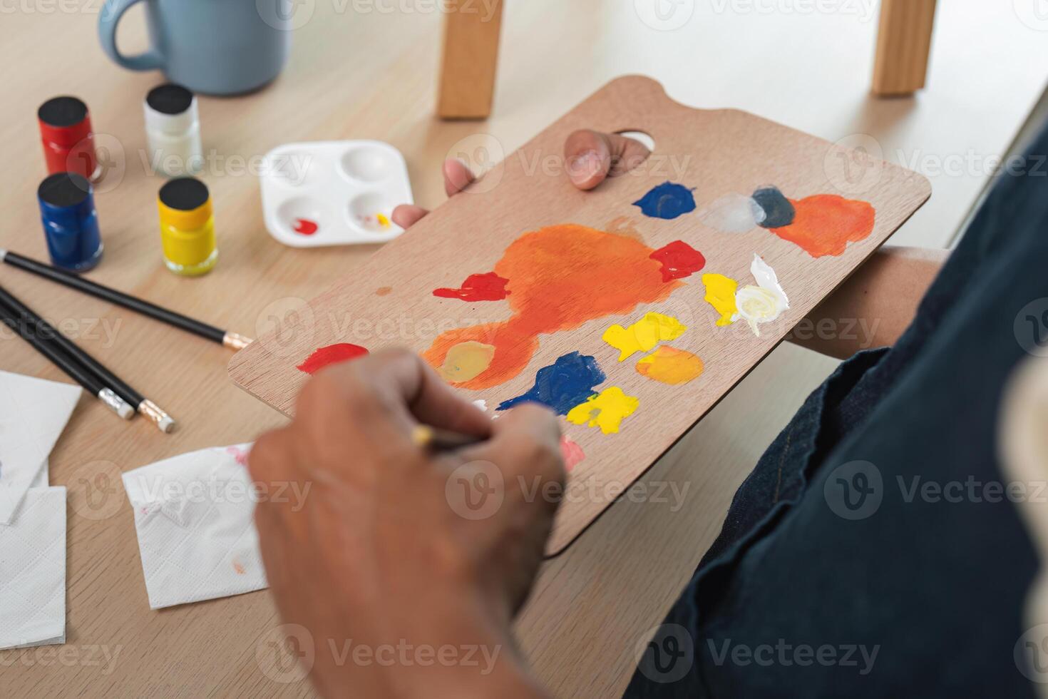 Artist Mixing Paint on Palette with Brushes and Paints on Wooden Table in Studio photo