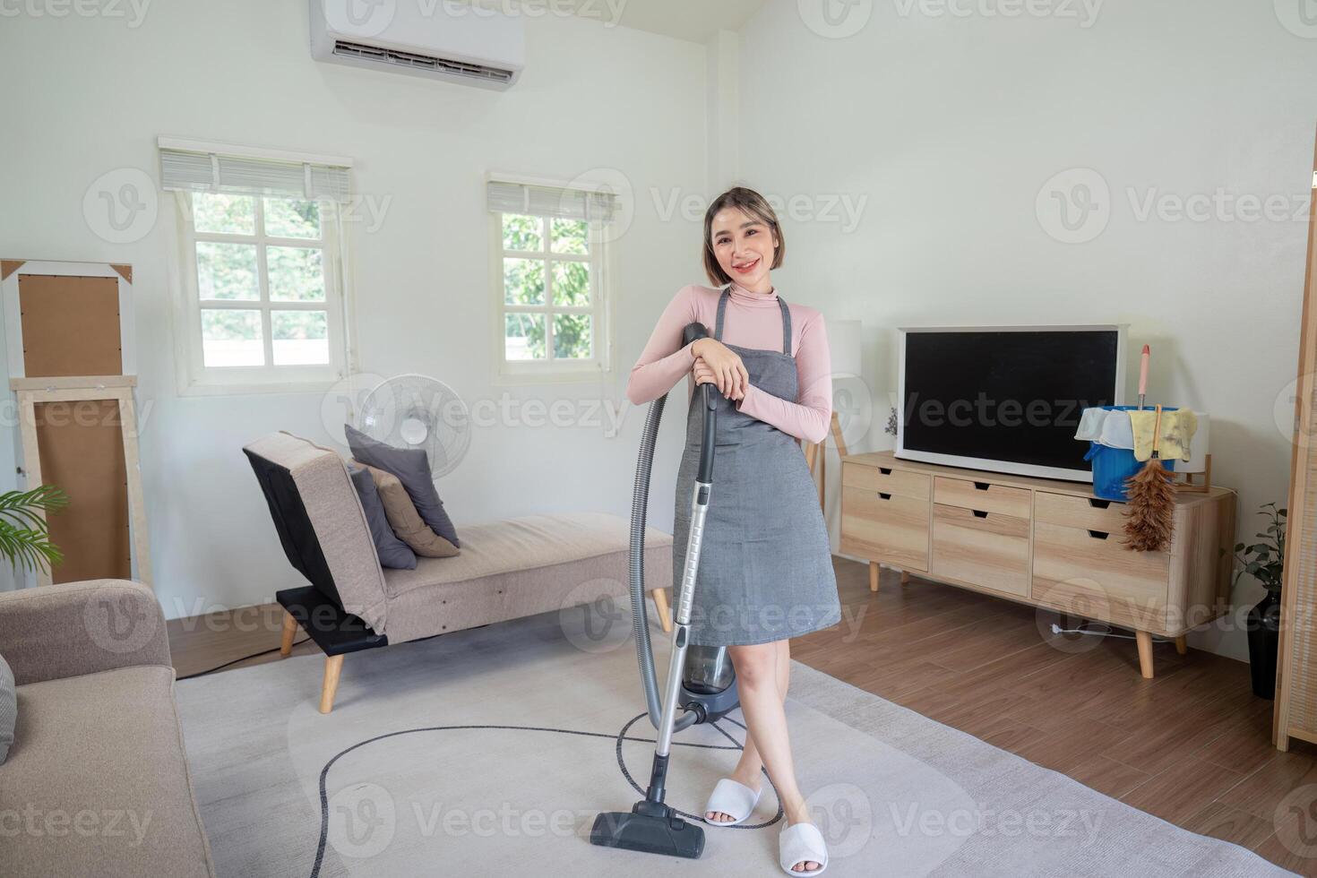 Woman Smiling While Holding a Vacuum Cleaner in a Modern Living Room with Minimalist Decor photo