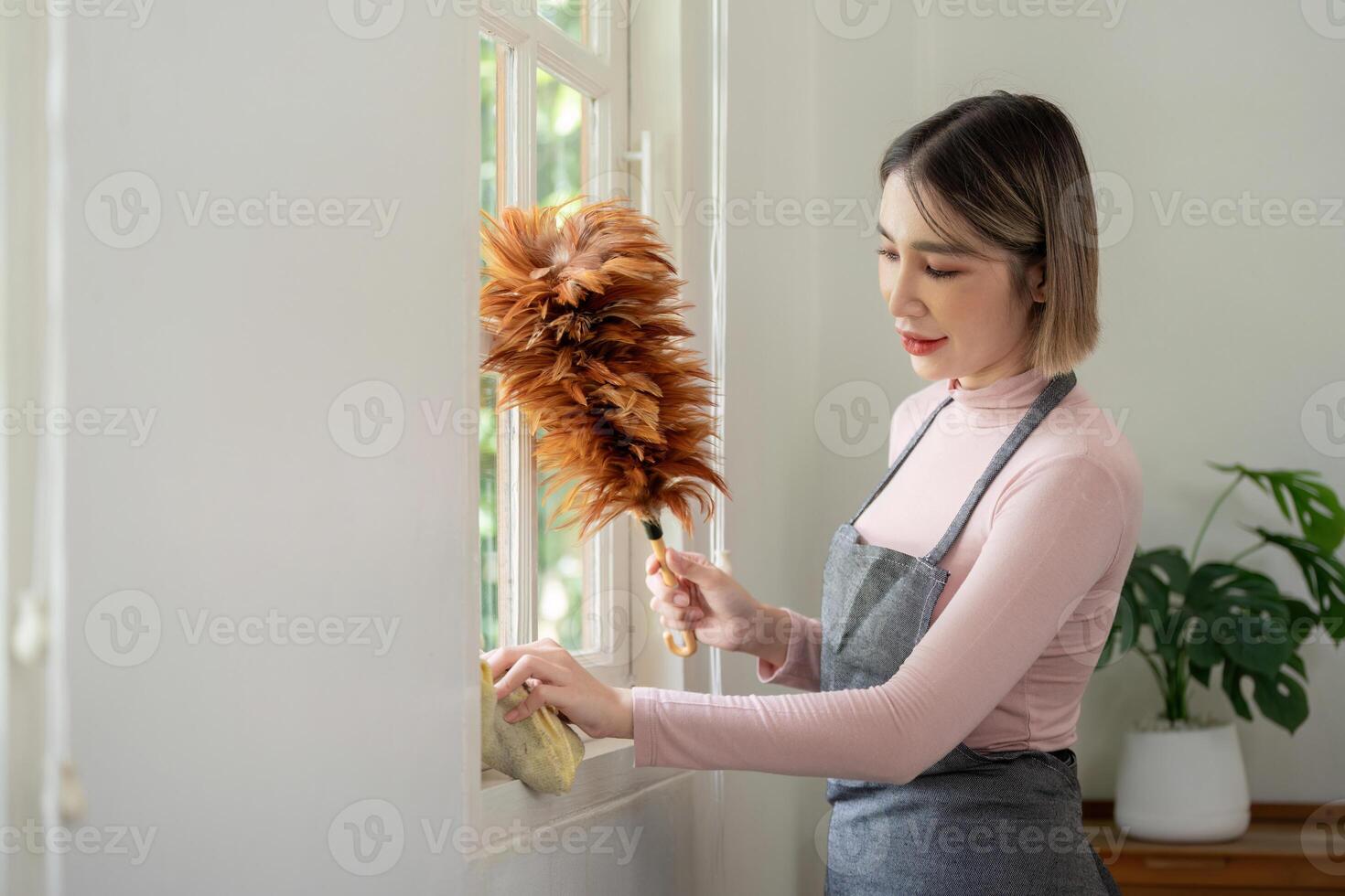 Woman Cleaning Window with Feather Duster in Bright Modern Home Interior photo