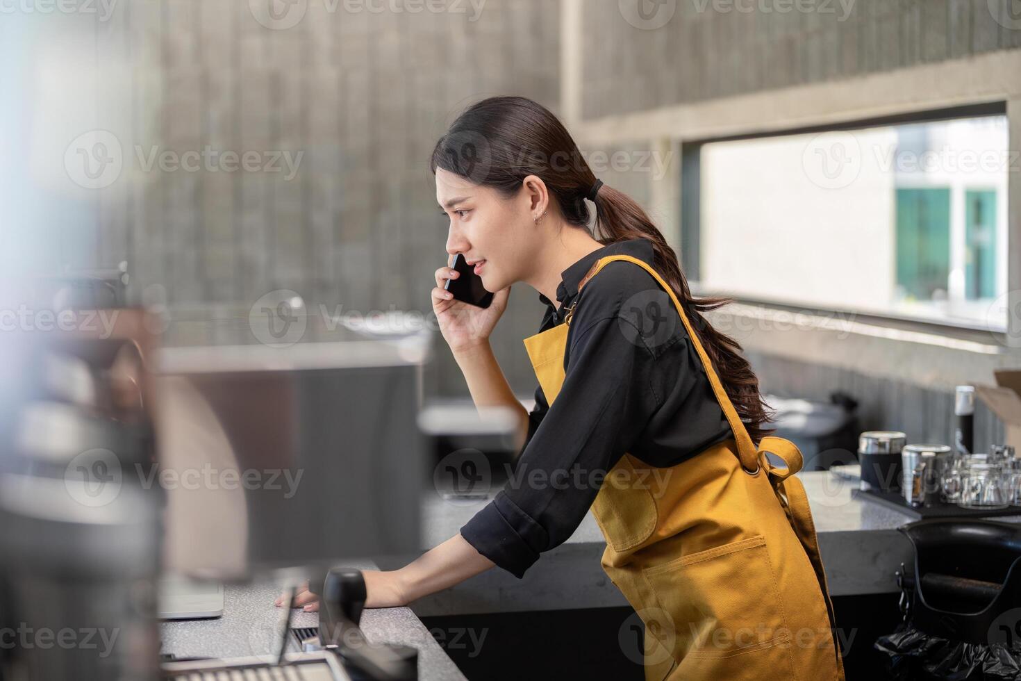 Young Female Barista in Yellow Apron Taking an Order Over the Phone in a Modern Coffee Shop photo