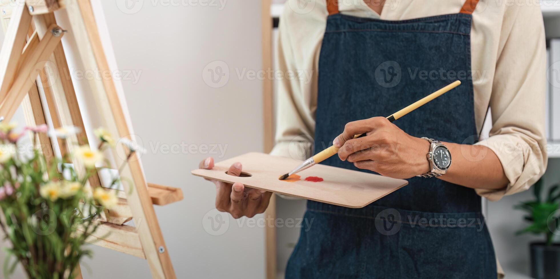 Artist Painting on Canvas in Studio Wearing Denim Apron and Holding Palette with Paints photo