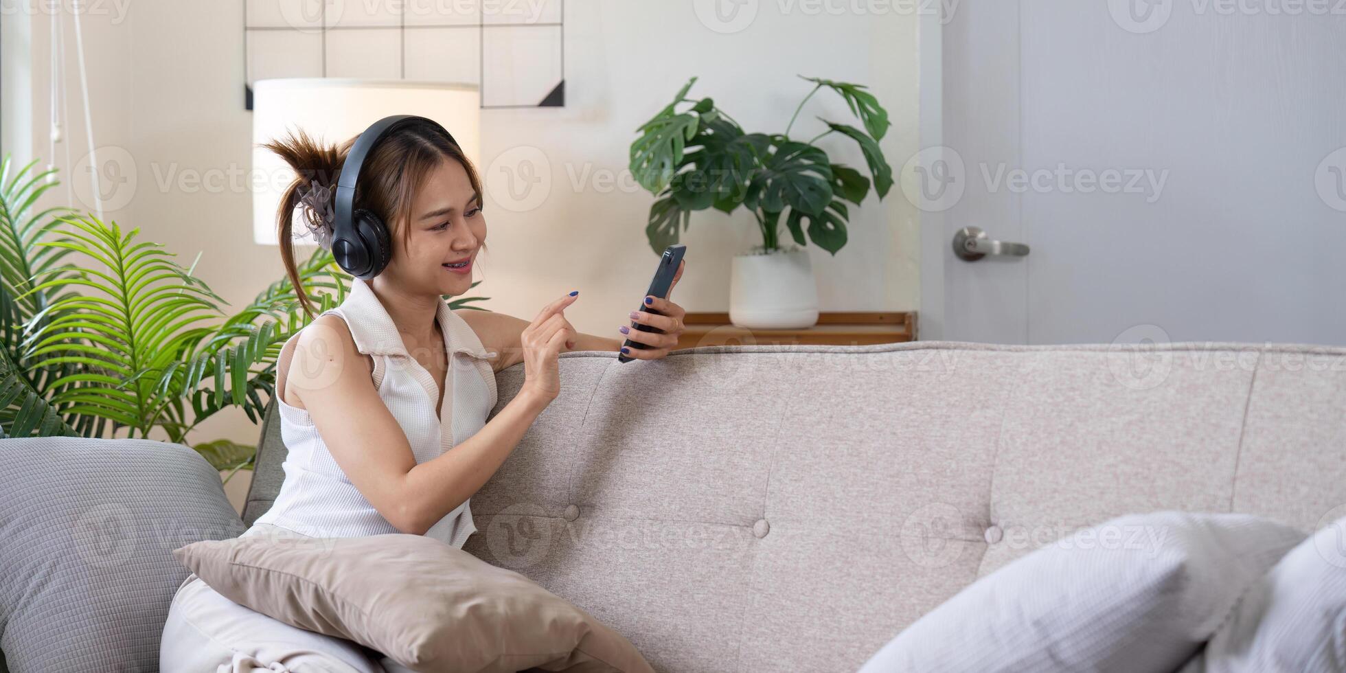 Young Woman Relaxing on Couch with Headphones and Smartphone in Modern Living Room photo