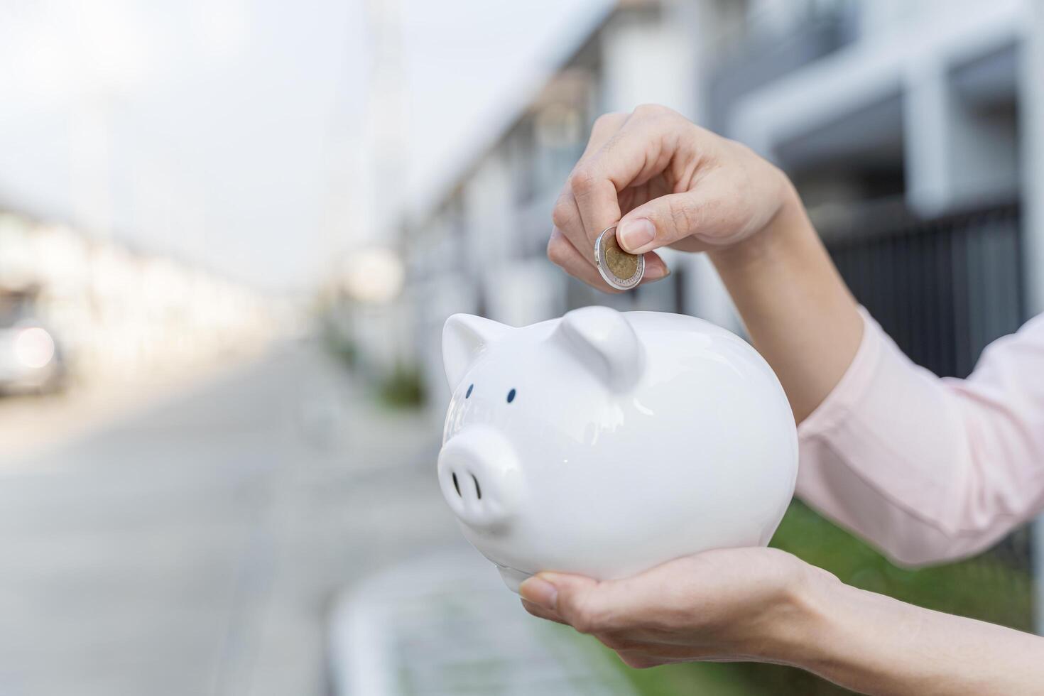 Woman hand hold a coin is save to the piggy bank with growing a interest and wooden home model for family in the public park photo