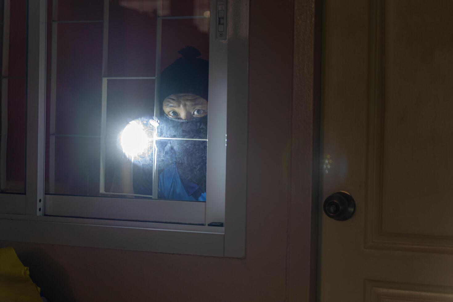 Thief Breaking House Window To Enter House.Burglar with flashlight looking through the window photo