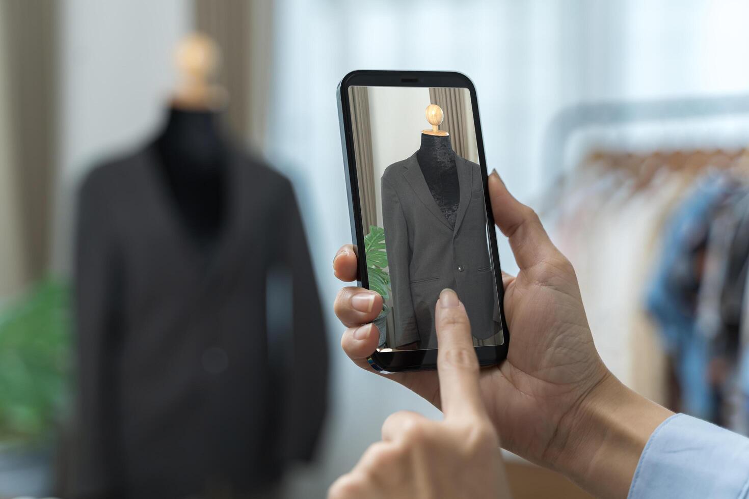 Close-up of a hand holding a smartphone to take a picture.woman seamstress standing next to mannequin with blue. photo