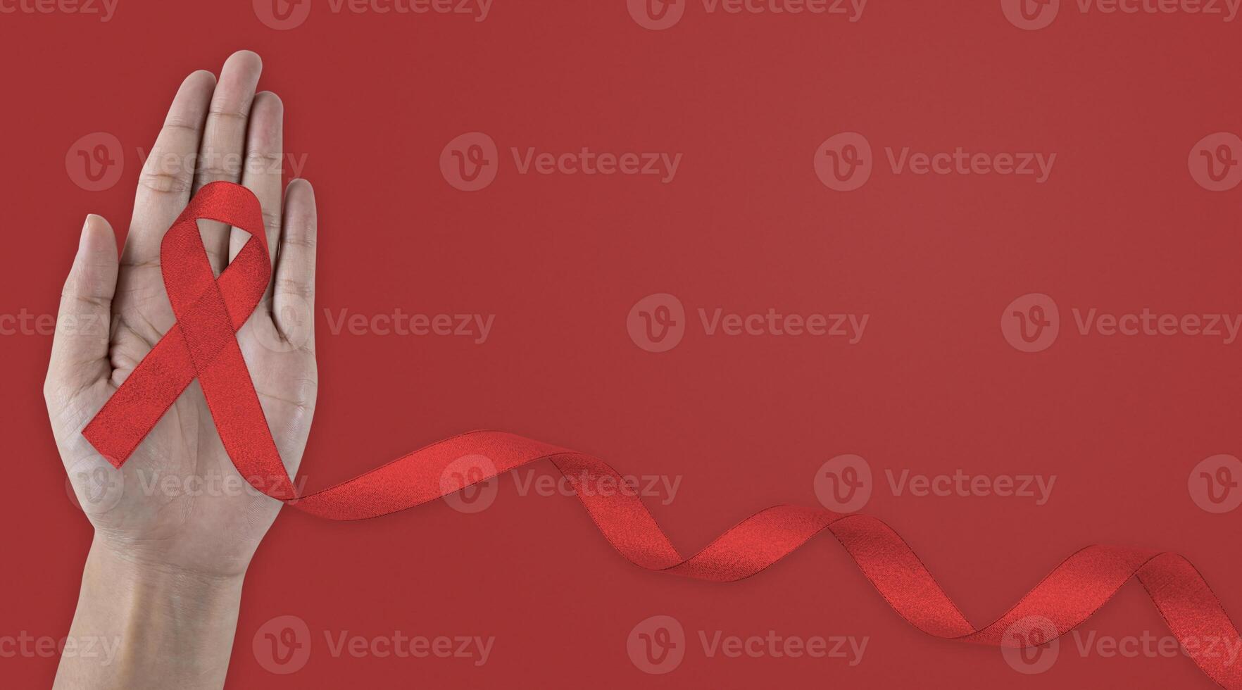 First person top view photo of cupped female hands and red ribbon symbol of aids awareness on isolated red background.