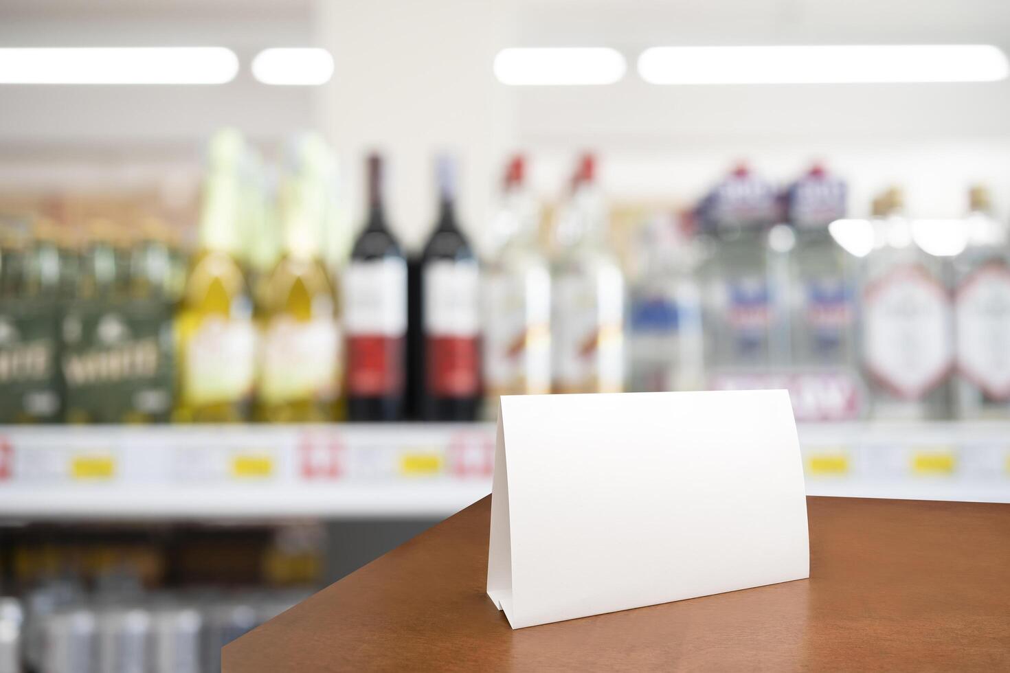 Blank paper table card on wooden table over bar background. Blurred counter has a wide variety of liquor bottles that are sold in supermarkets. photo