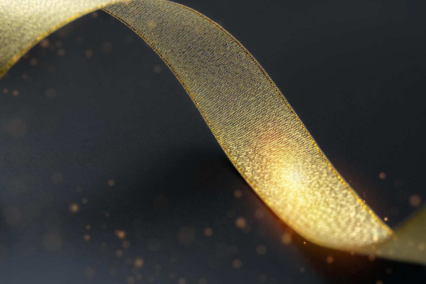 Golden ribbon isolated on black background and texture. Gold gift wrap ribbon on black fabric background. Holiday, celebration. With copyspace. photo