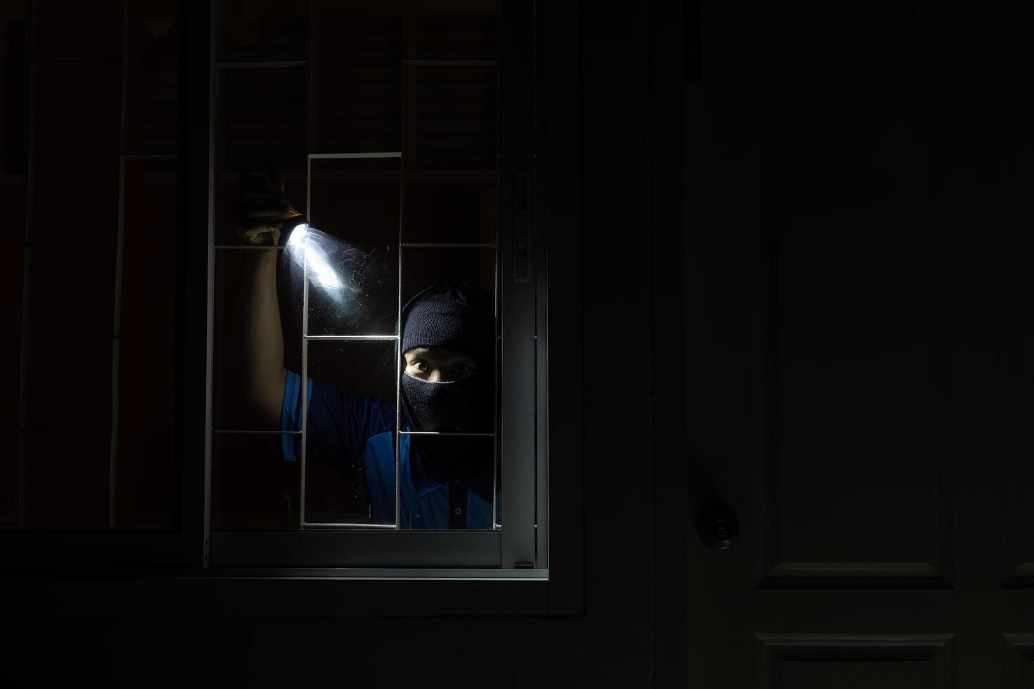 Burglar breaking in to home in night through window. Burglar at night with flashlight at window of the house photo
