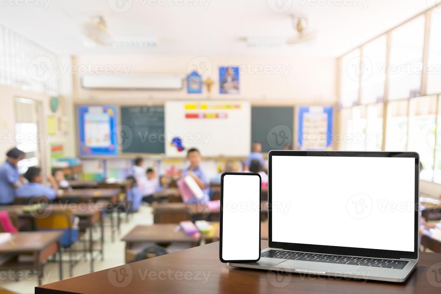 Children students in classroom background. Education software website technology ads concept. Front view, blank screen of black digital laptop and smartphone photo
