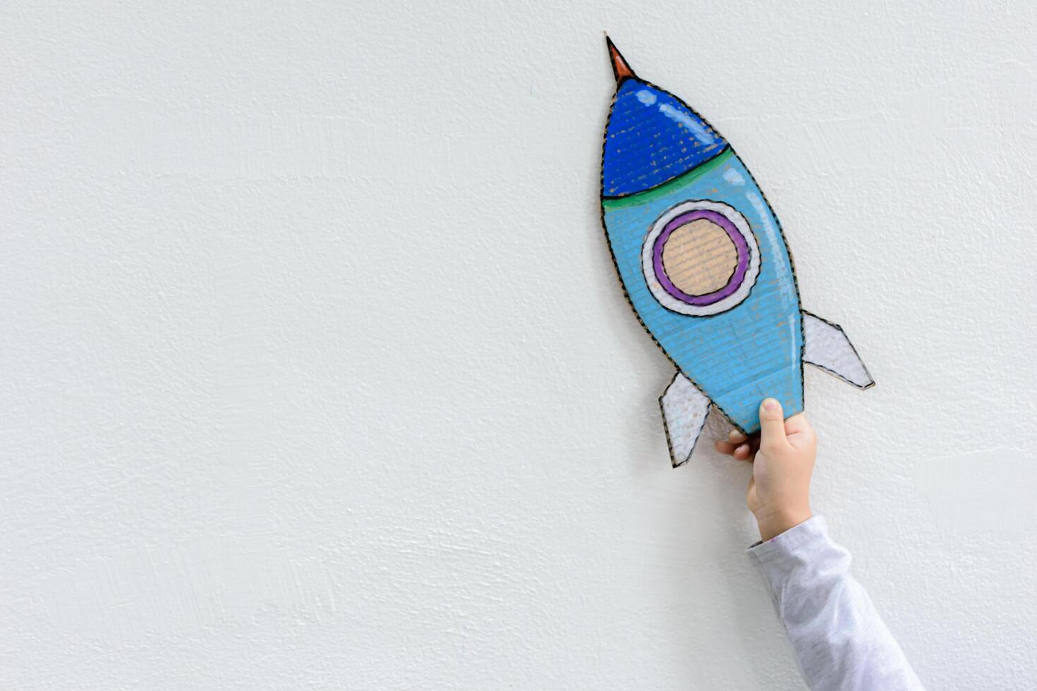 Young Asian boy holding rocket on raised hand standing in art class in backlit with imagination the astronaut and space rocket photo