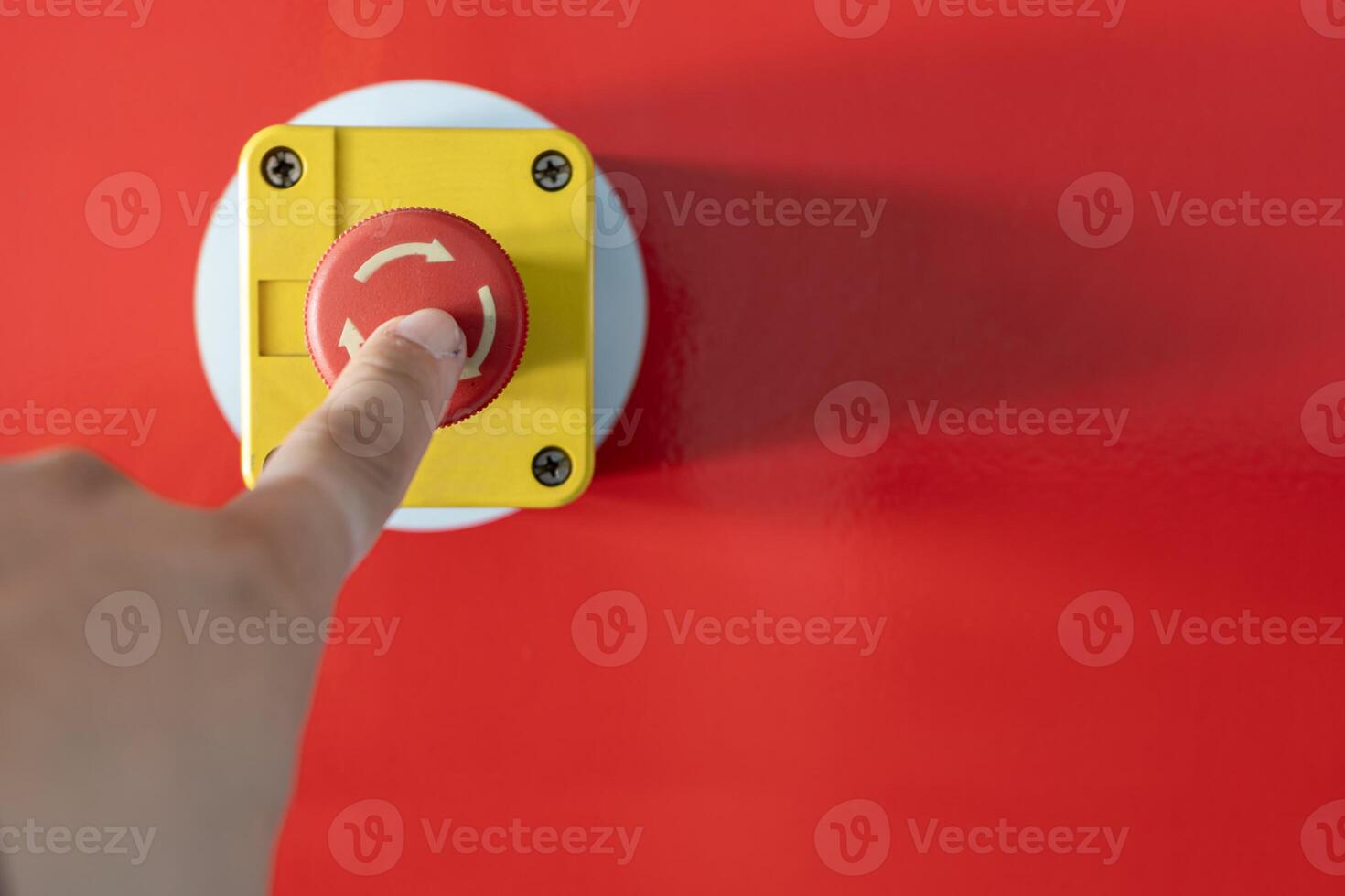 An industrial emergency stop button with a finger pressing down photo