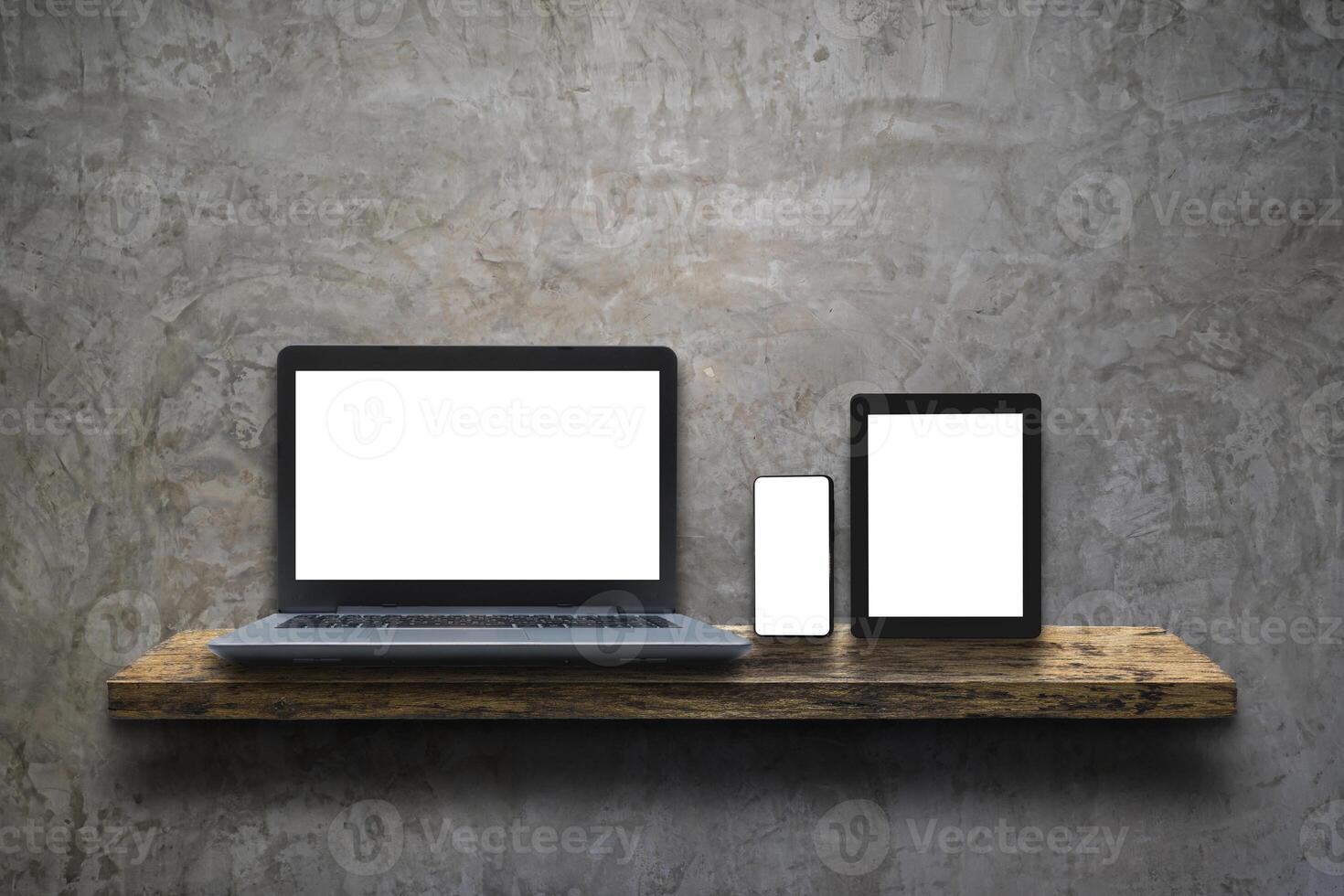 Laptop, mobile phone and digital tablet pc on wooden shelf over white concrete wall background. Rustic rough wooden plank with nature color. photo