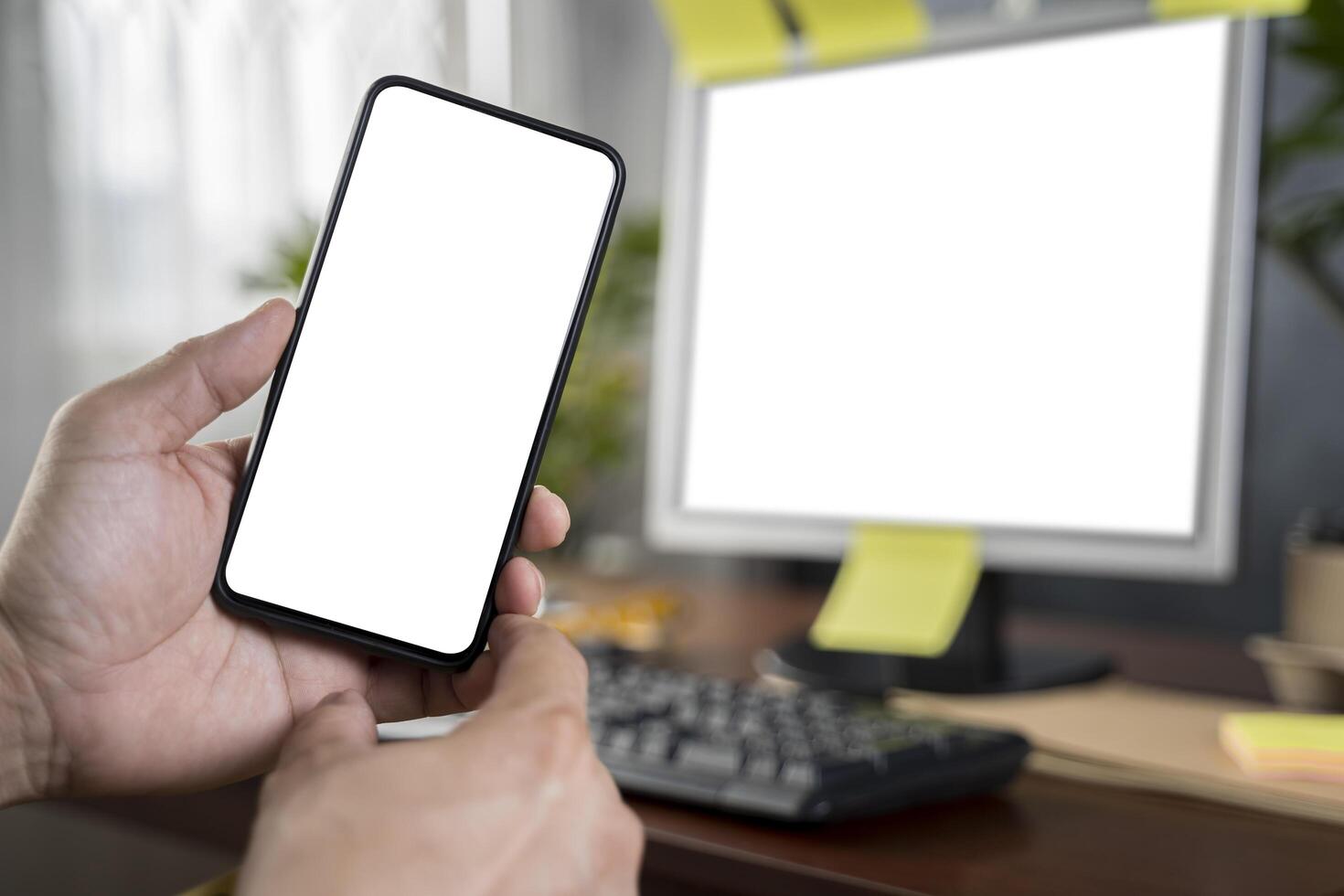 Close up with man's hand holding smartphone in front of laptop, blank screen of smartphone and laptop. photo