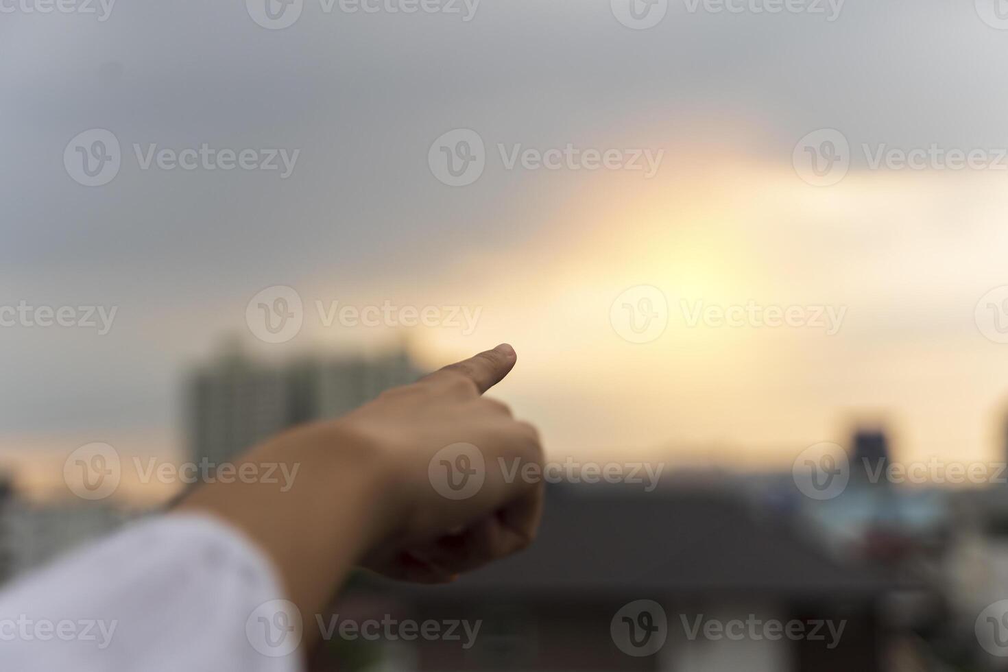 Close-up female hand with index finger up on a background of golden sky with clouds, copy space. photo