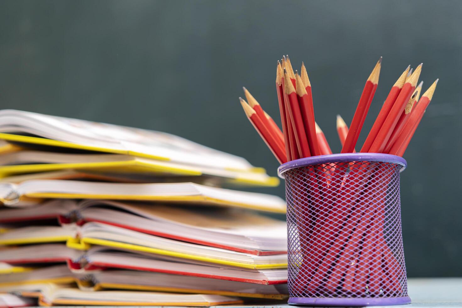 Concept to teacher's day. Pens, pencils, books on table, against the background of chalkboard. Back to school photo