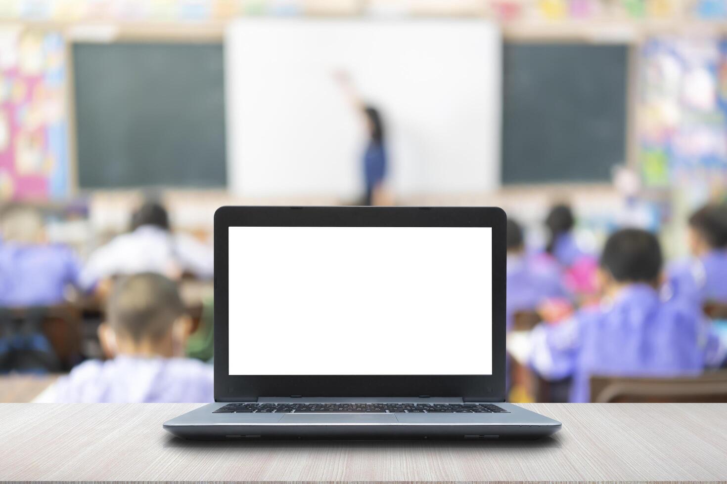 Computer on the table, blur image of children in the classroom as background. photo