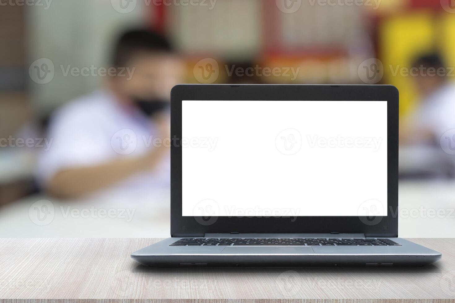 The laptop is placed on the teacher's desk. Blurred background image of a child's classroom photo
