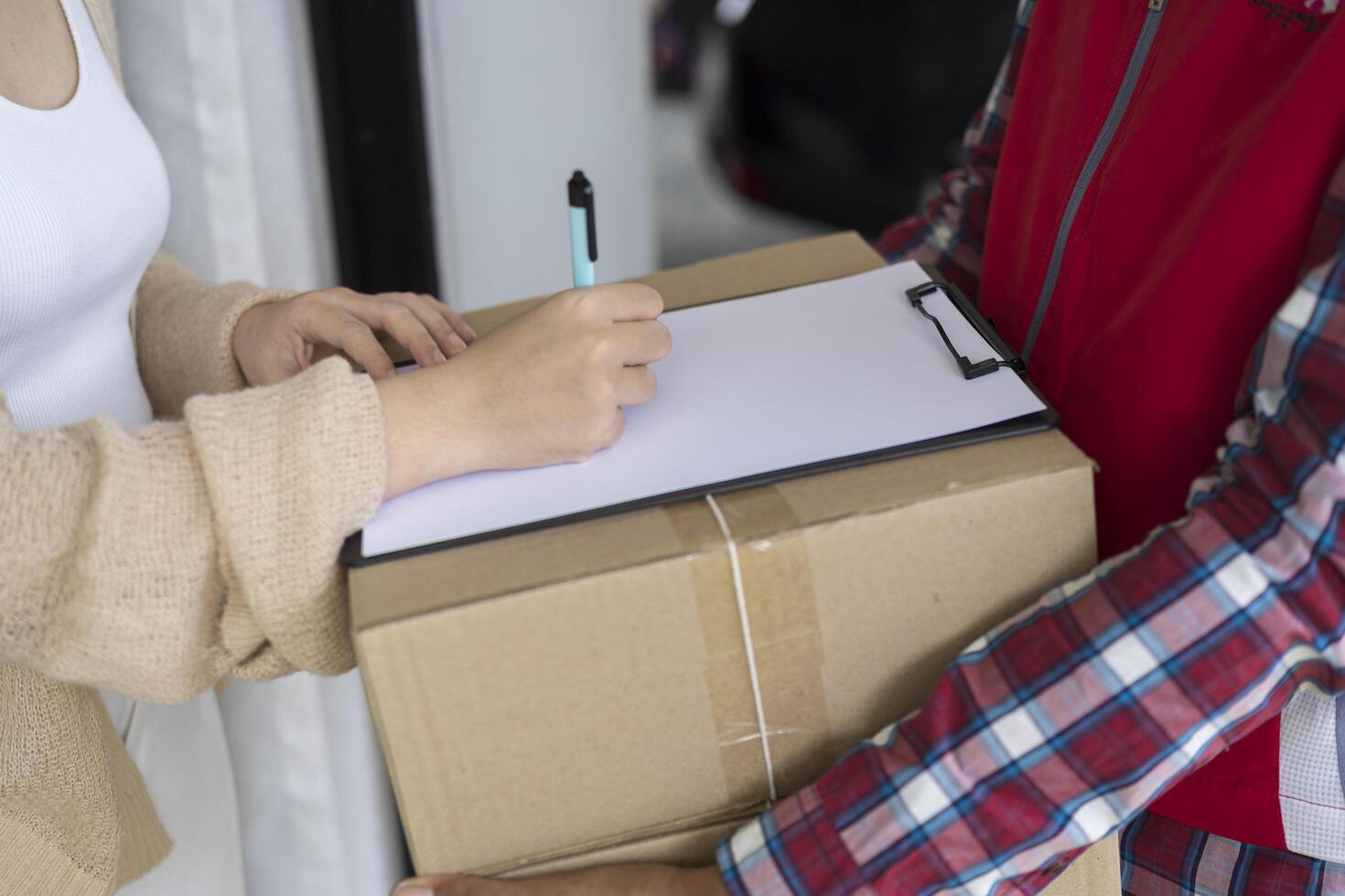 Young courier delivery man in red uniform holding a parcel cardboard box delivering package and woman putting signature in document photo