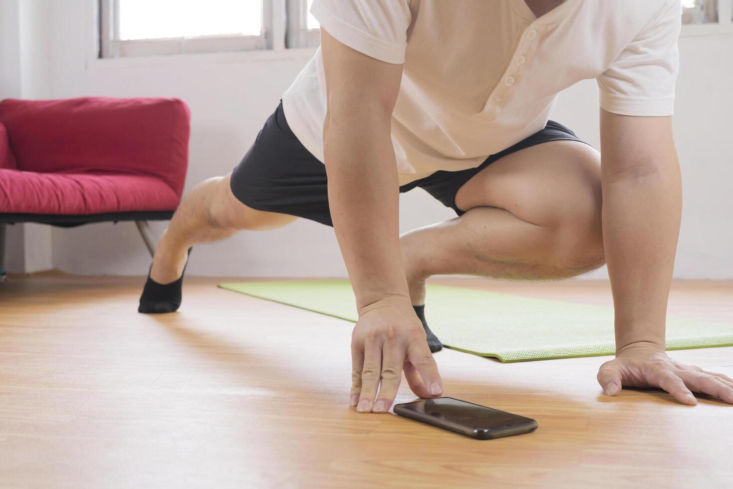Muscular Athletic Fit Man in T-shirt and Shorts is Doing Mountain Climber Exercises While Using a Stopwatch on His Phone photo