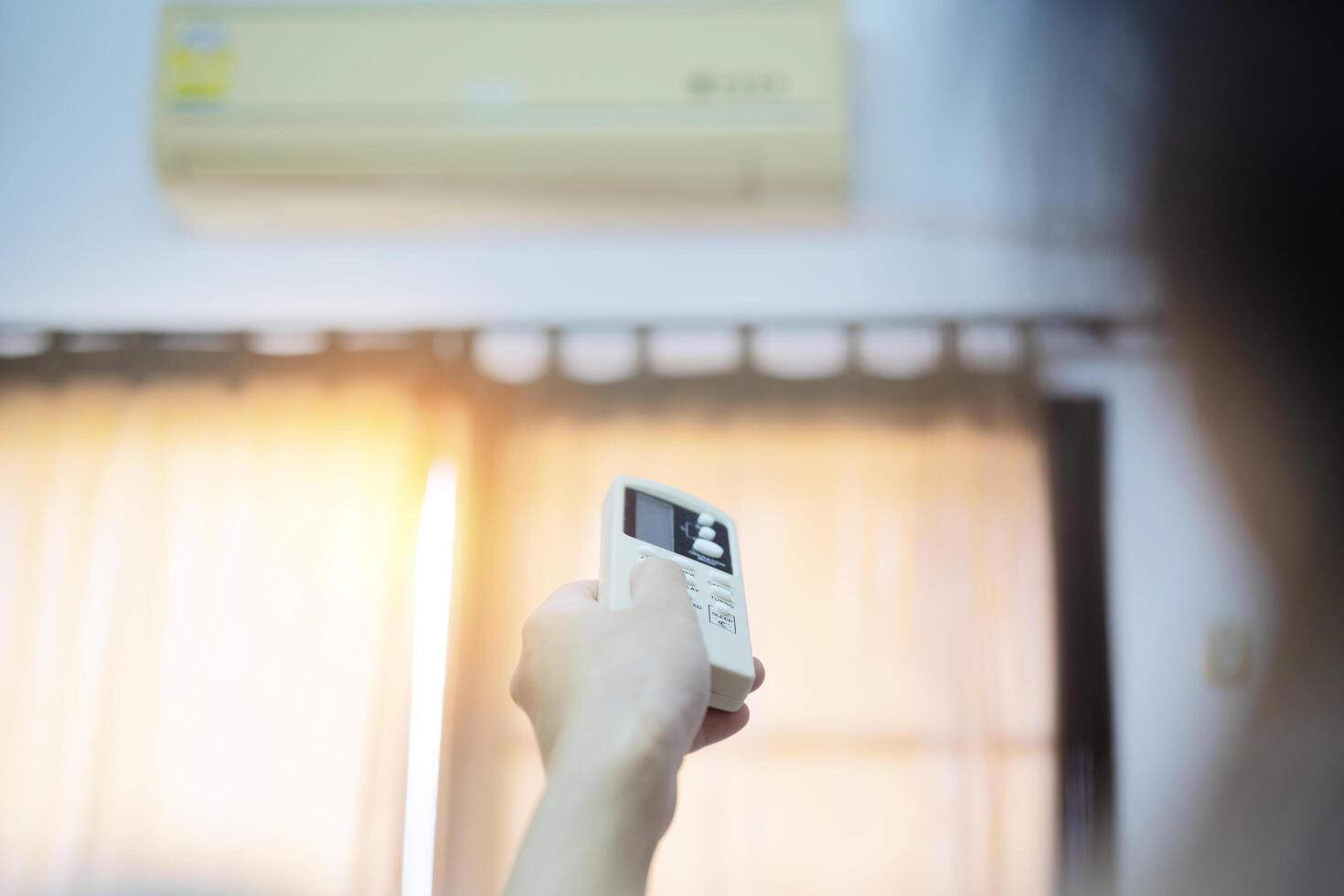 An air conditioner in a room with a young person using a remote control is turning on photo