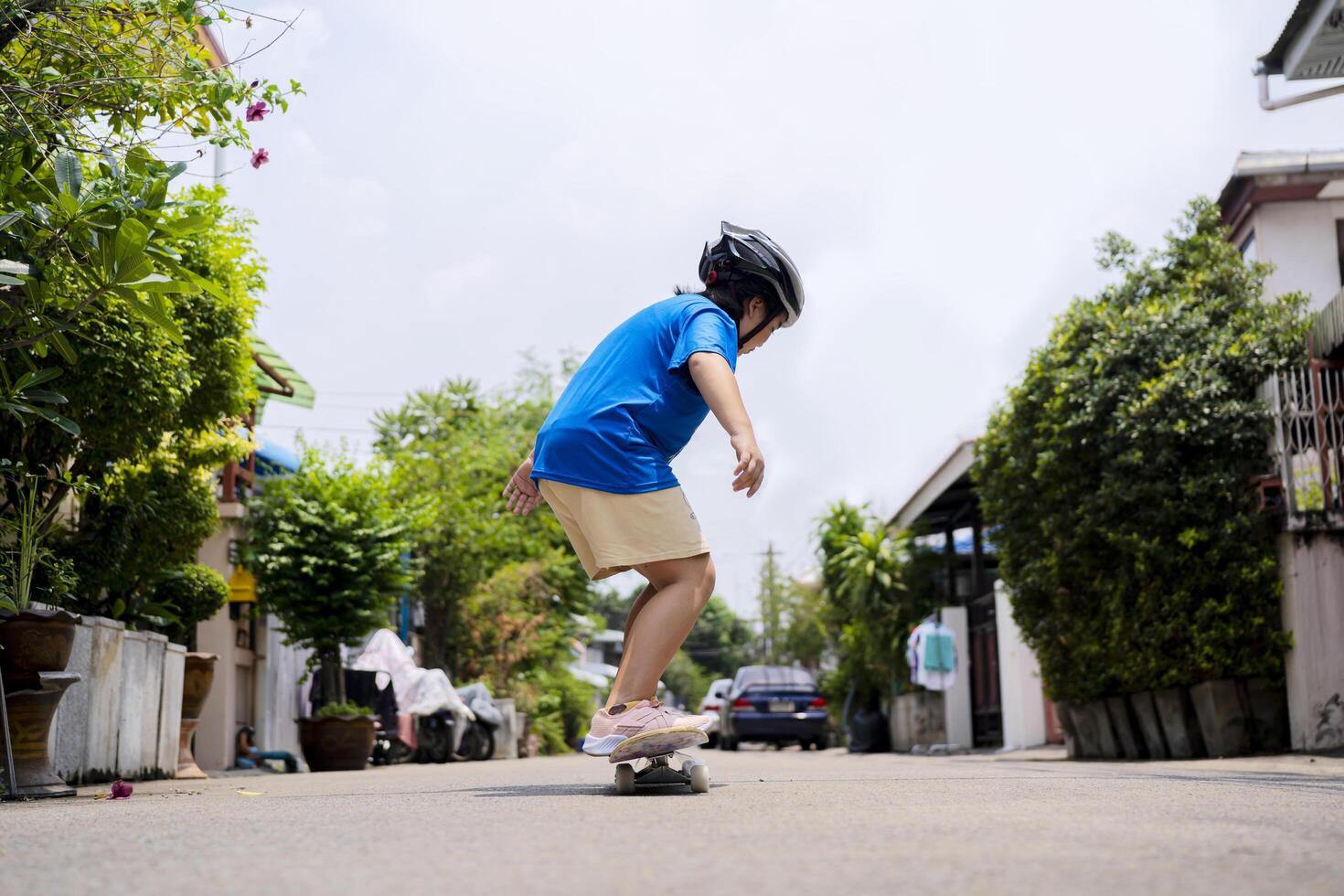 An Asian girl stands on a skateboard with a helmet on the village road. photo