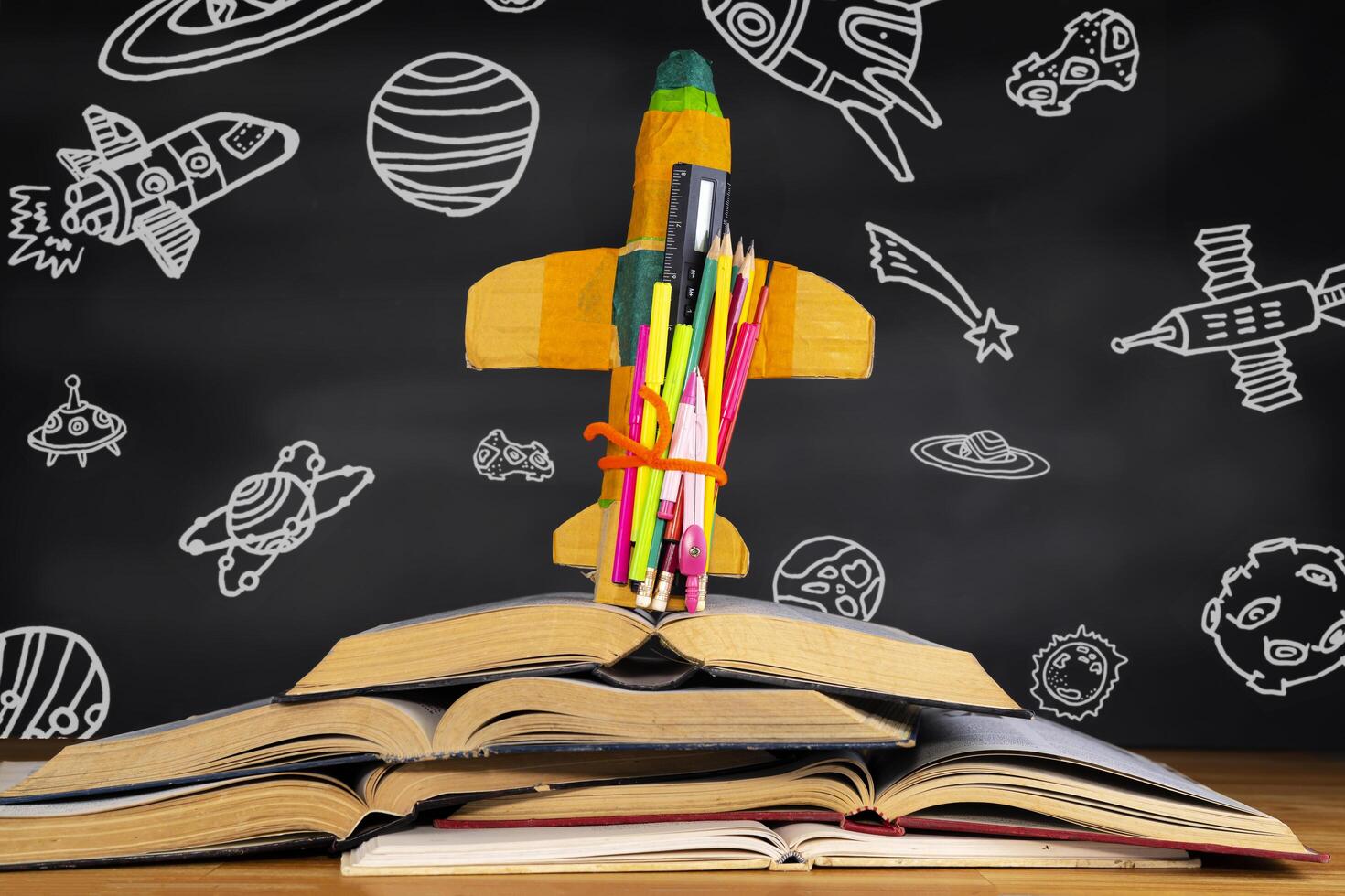 rocket placed over a book in front of a blackboard depicting space objects in the classroom. photo