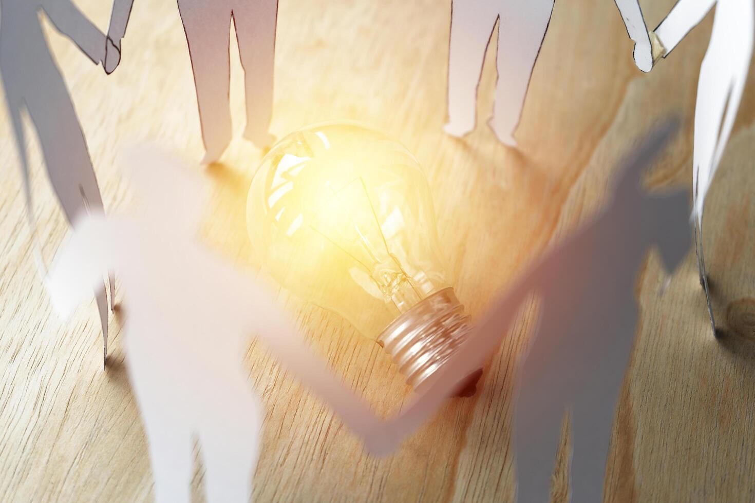 A group of diversify paper chain people surrounding a light bulb. photo