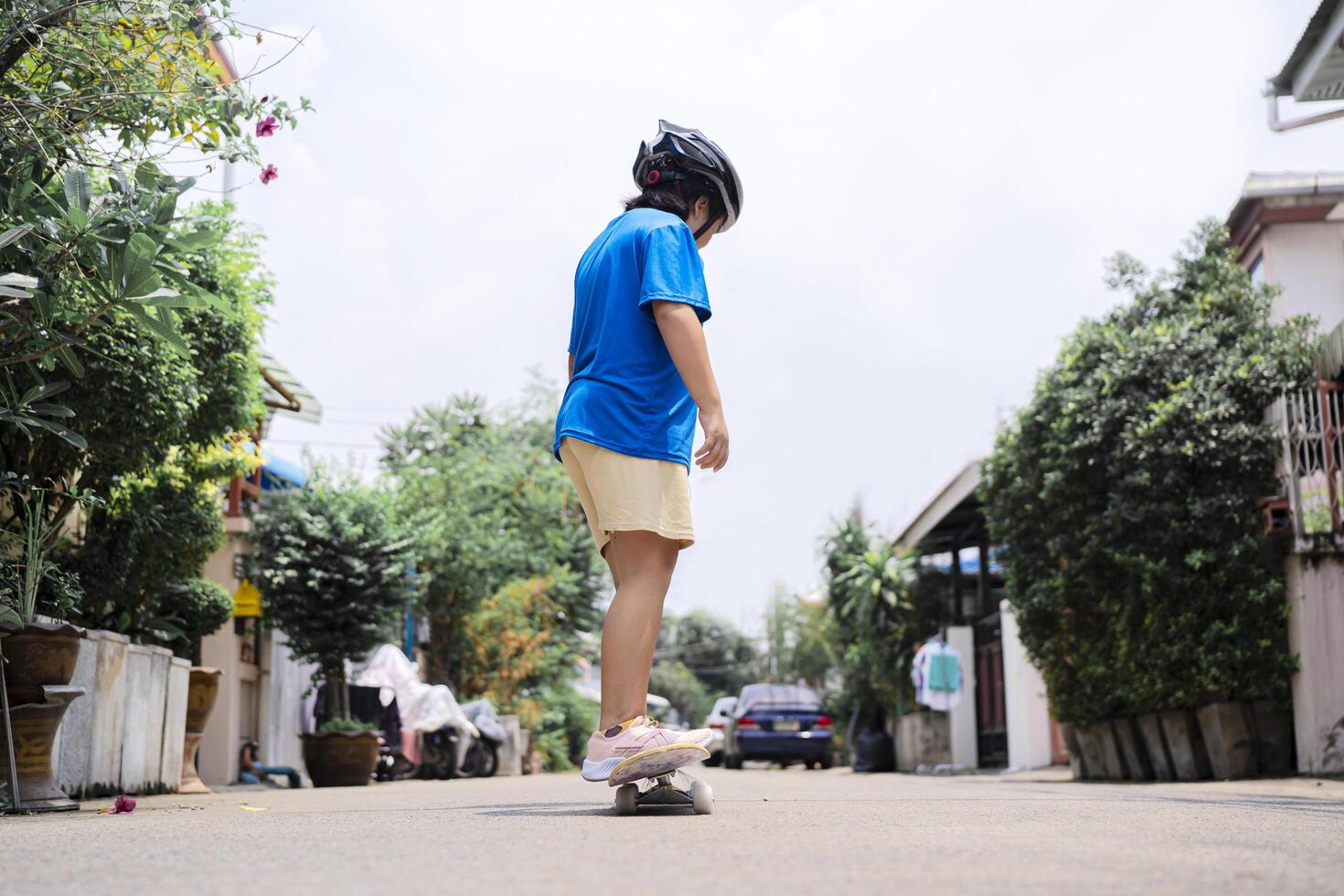 An Asian girl stands on a skateboard with a helmet on the village road photo