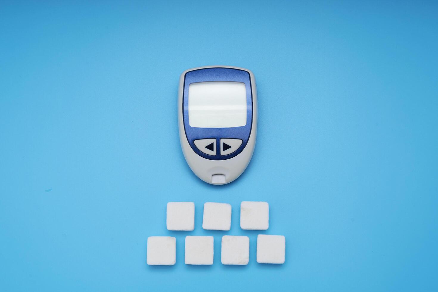Sugar cubes and Glucose meter on blue background photo