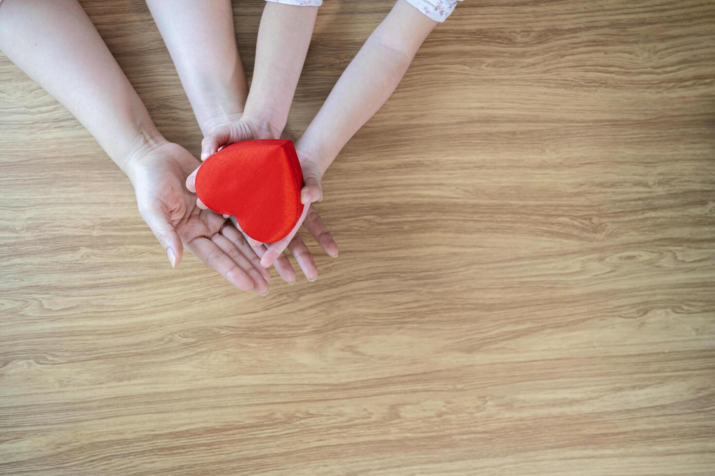 A red heart gift box in the hands of the child and mother on a white wooden background The concept of love photo