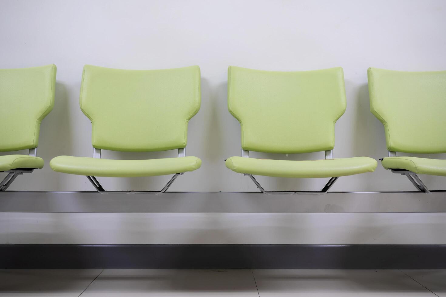 Row of green office chairs standing in corridor or conference room, empty dark seats arranged in line in boardroom, range of basic stools in front of white wall. Interview, recruitment concept photo