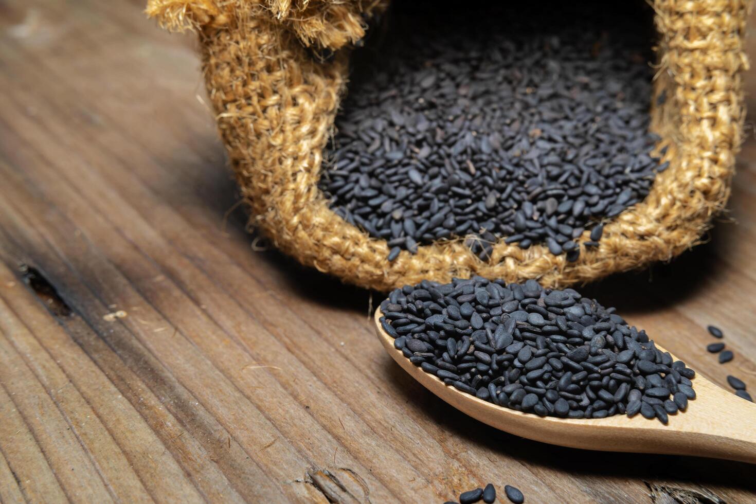 Heap of black Sesame close-up shot on a wooden spoon and in a sack, wooden background photo