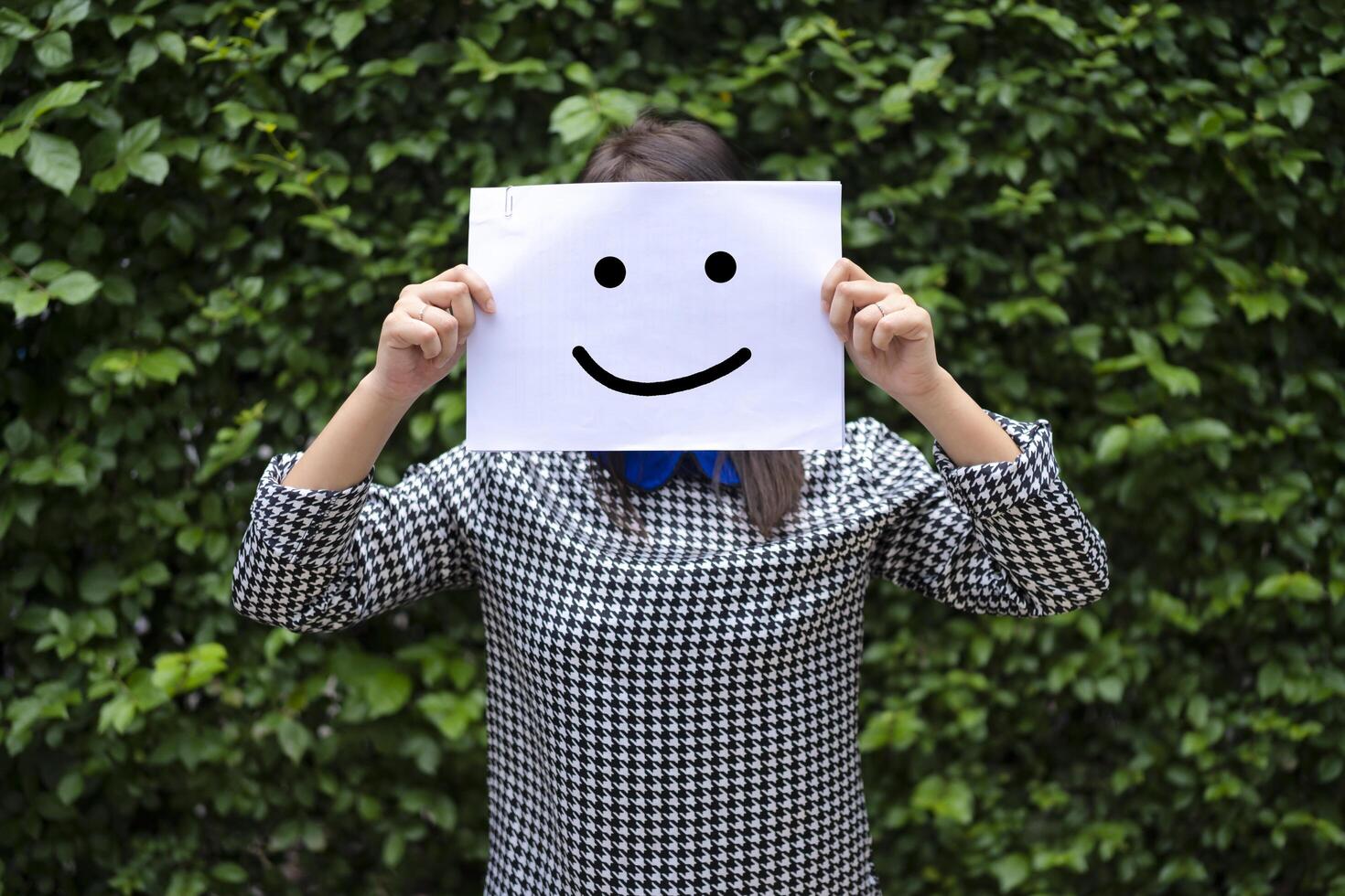 Girl holding paper on her head smiling face on the street, Leaf wall background photo