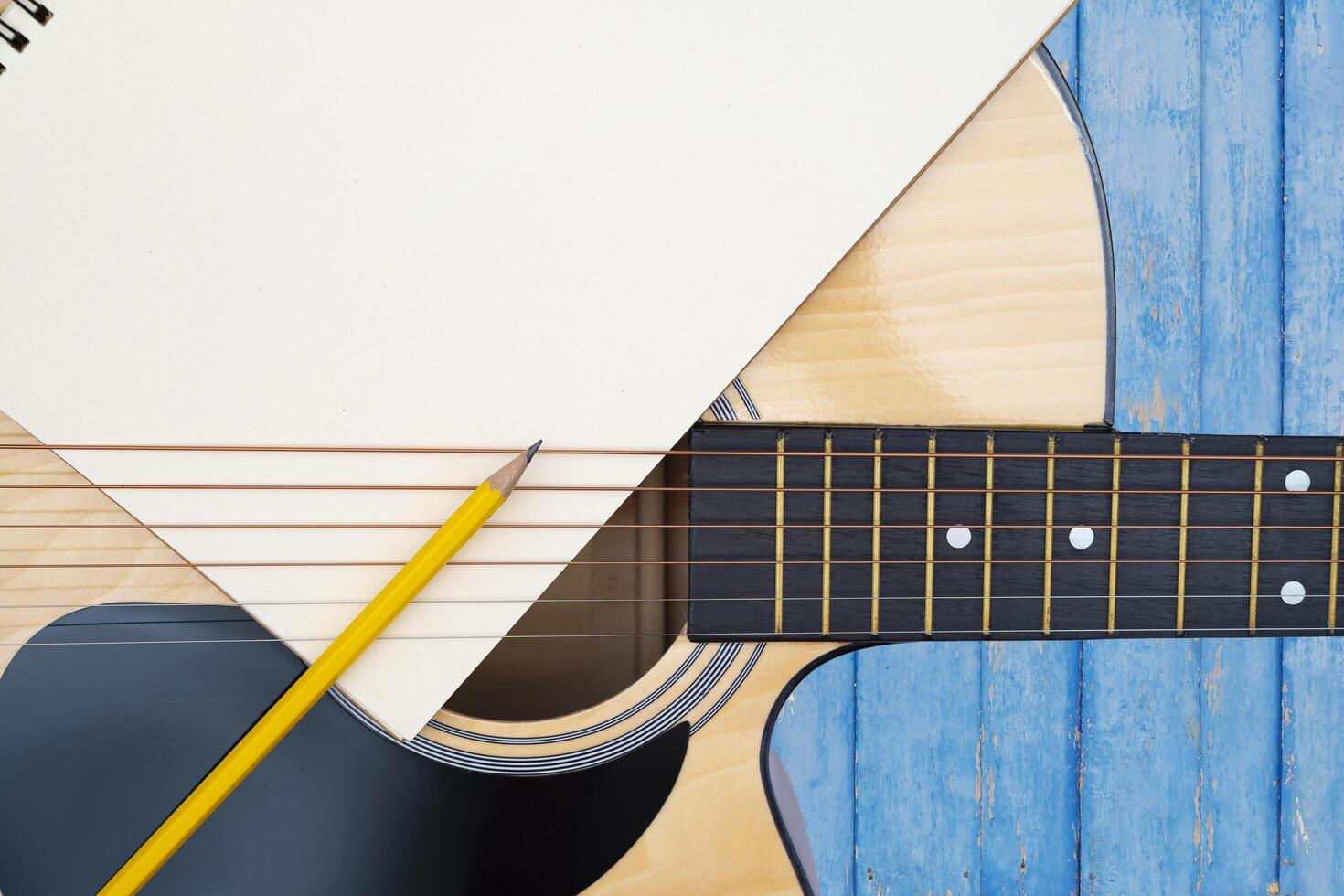 Acoustic guitar on blue background, The guitar body pattern is wood grain. Notebook and yellow wooden pencil photo