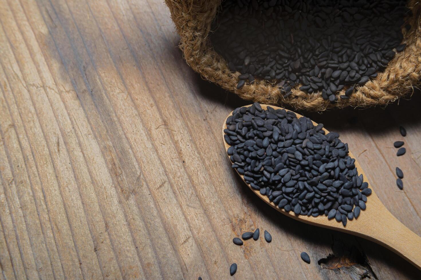 Heap of black Sesame close-up shot on a wooden spoon and in a sack, wooden background photo