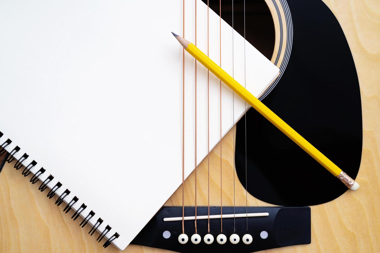 Acoustic guitar on white background, The guitar body pattern is wood grain. Notebook and yellow wooden pencil photo