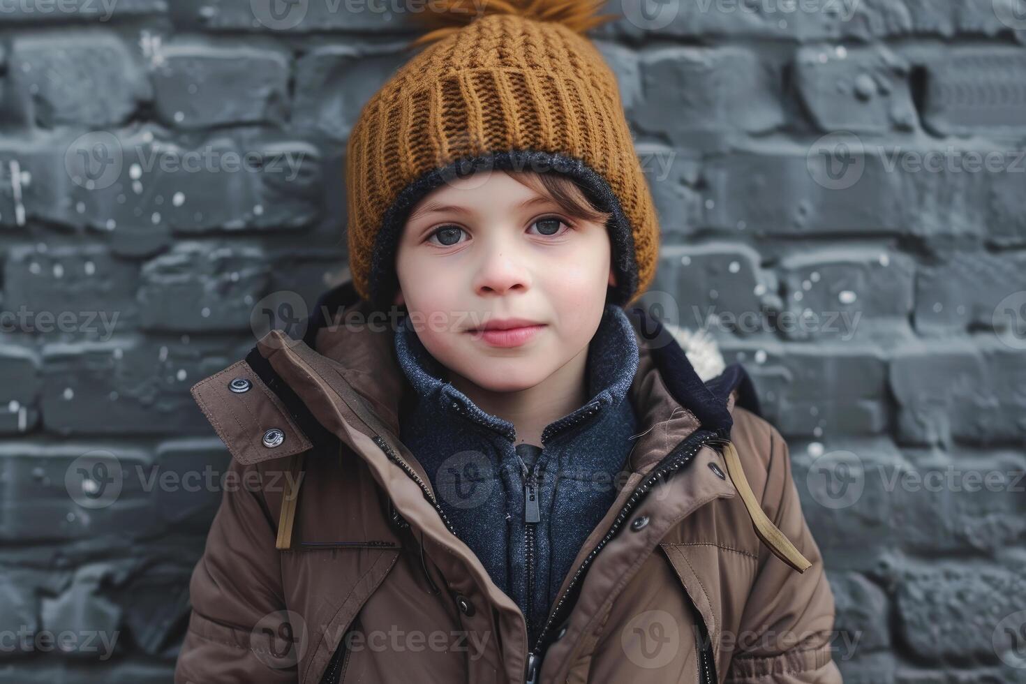 Young boy wearing winter clothes standing in front of grey wall photo