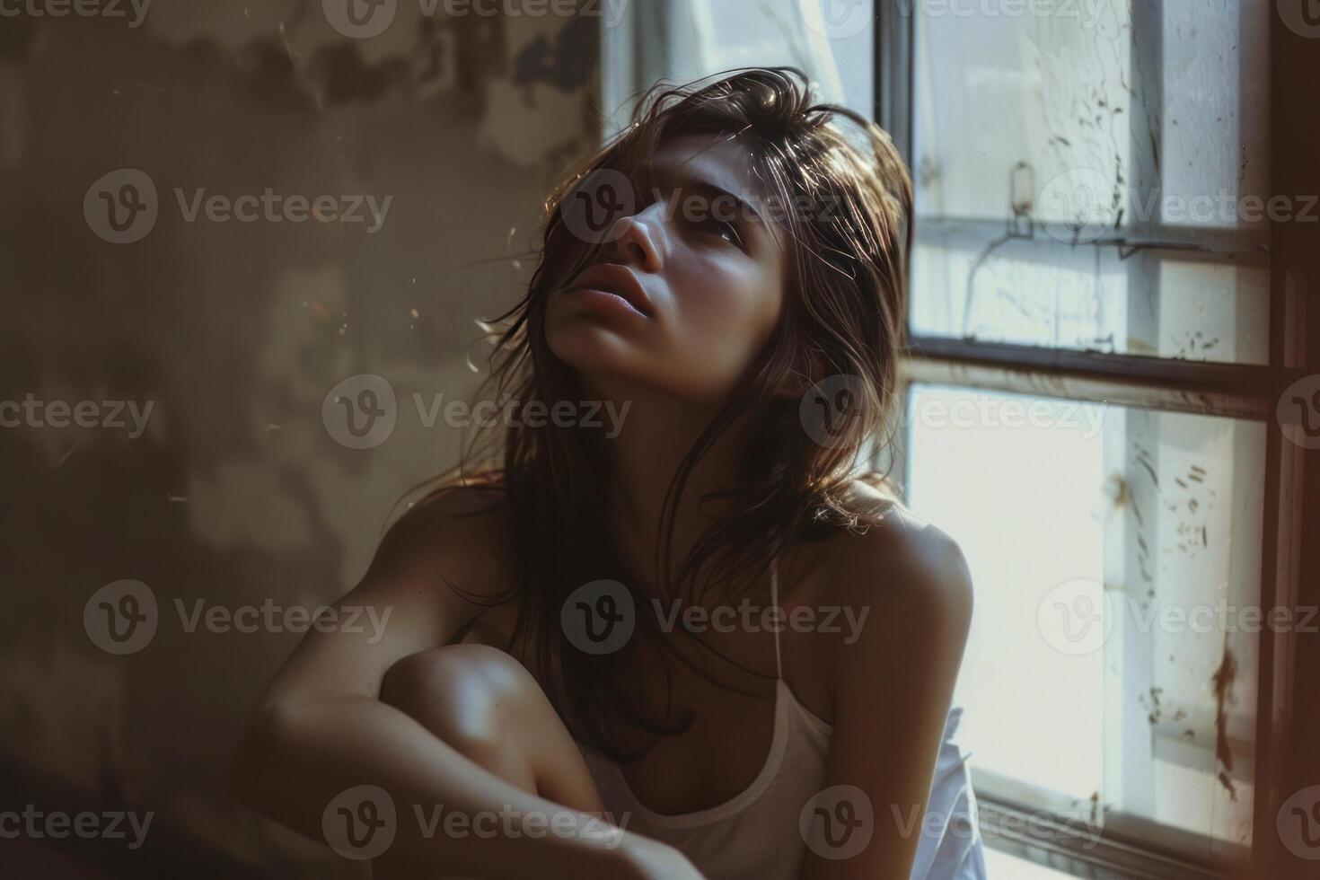 Contemplative young woman by window light photo