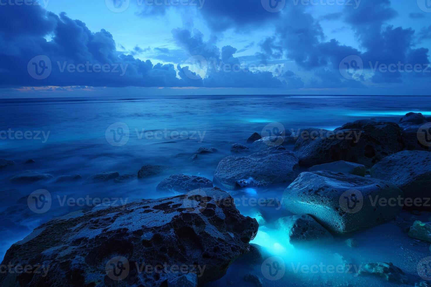 Bioluminescent ocean waves crashing on rocks at twilight photo