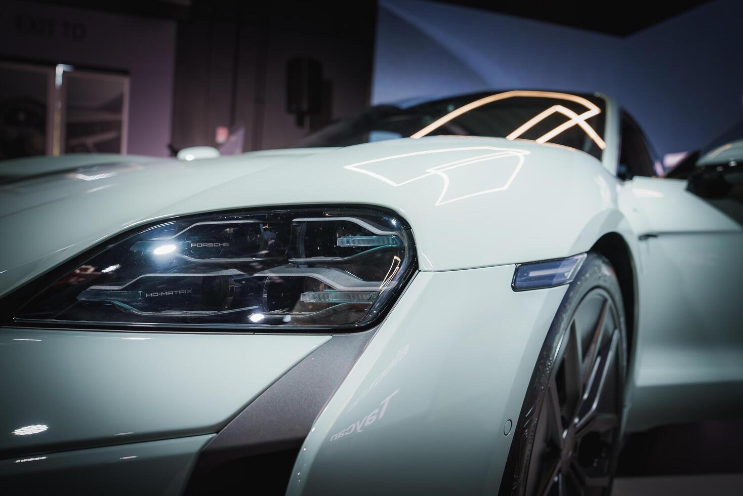 Sleek, modern car in glossy white finish. Close up of front left side reveals luxury design, LED headlight, and alloy wheel. Indoor setting with ambient lighting. photo