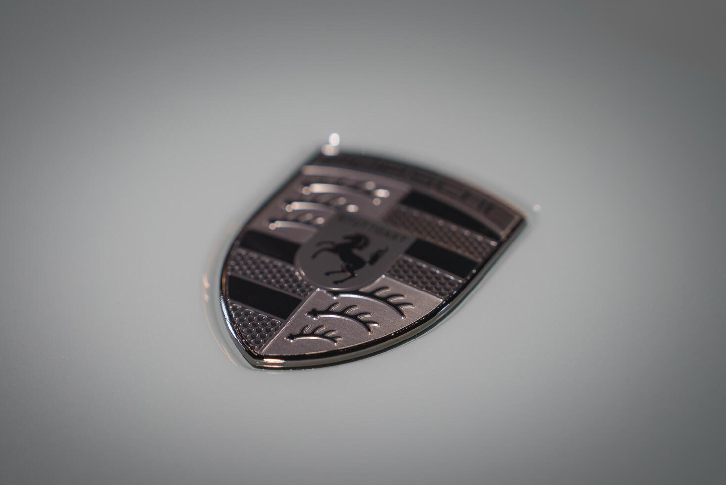 Metallic logo emblem with horse figure design, shield shape, patterned background, blurred setting. Symbol of speed and power, possibly from a car brand. photo