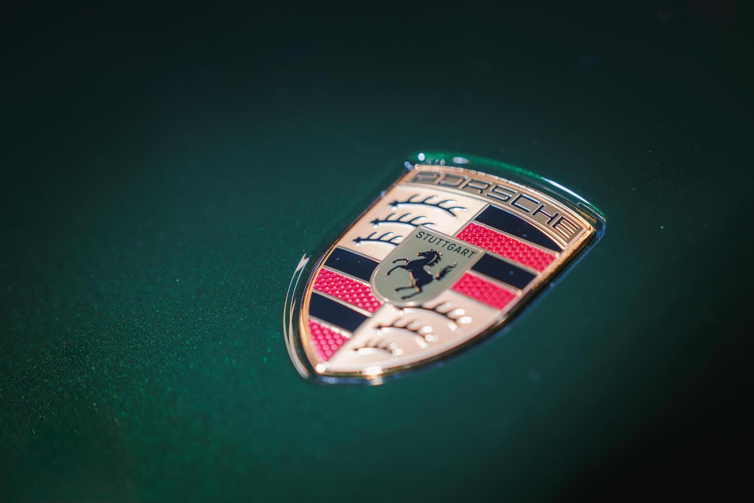 Close up of Porsche emblem with horse at center from Stuttgart, Germany. Detailed design against dark green background. Blurred focus highlights metallic shine. photo