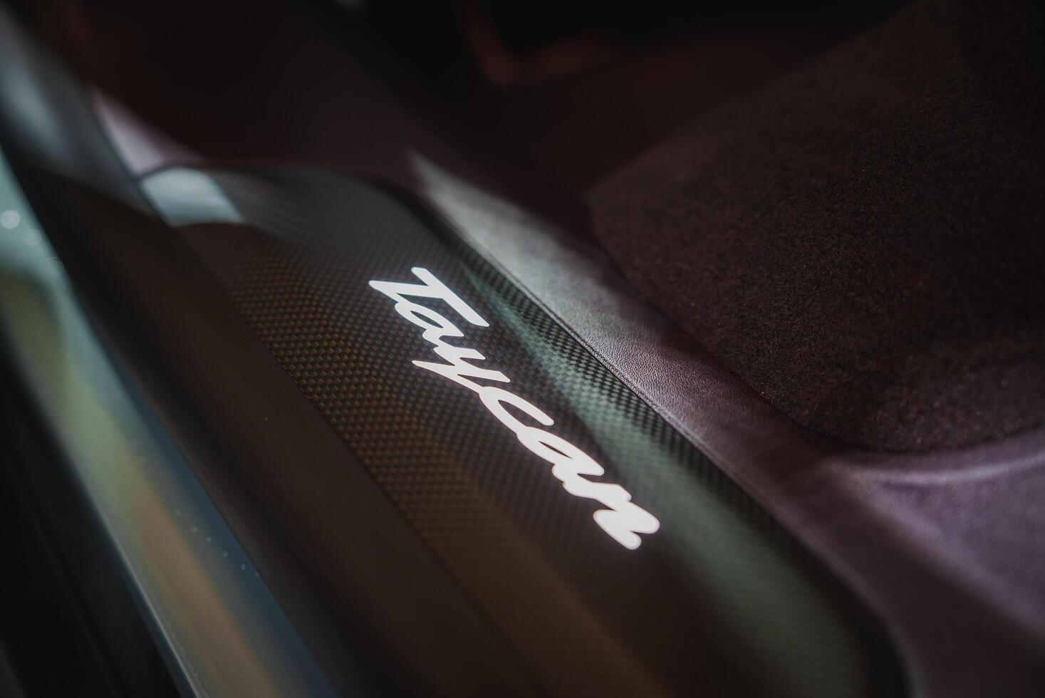 Close up of a Taycan branding element on a vehicle, hinting at luxury and high performance. Dark background, carbon fiber texture. photo