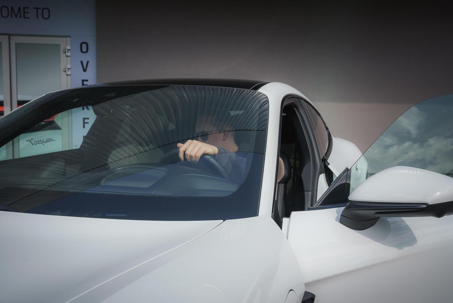 Close up view of white car with driver's side door ajar, hand gripping steering wheel. Sleek modern car in showroom setting. photo