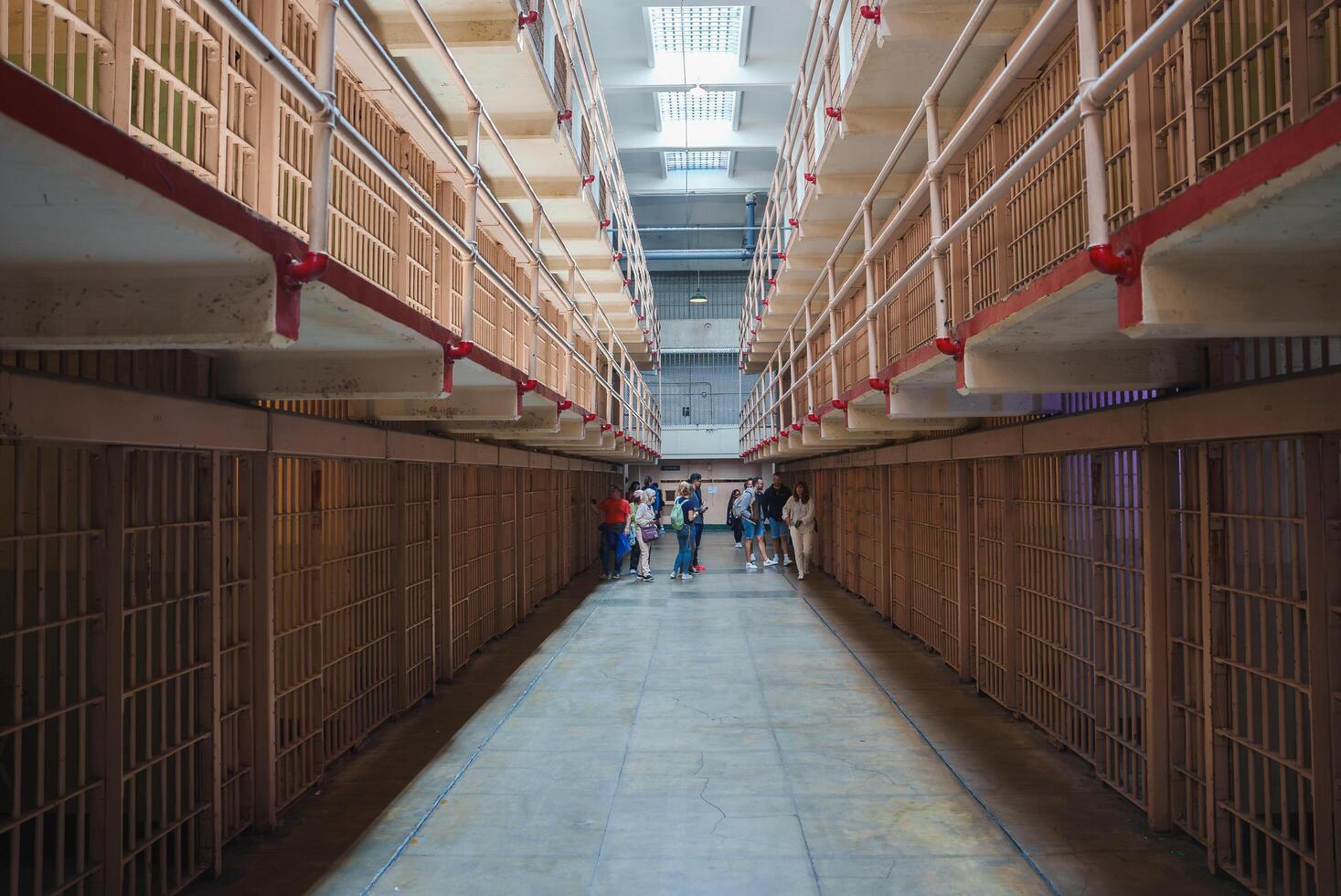 Interior view of Alcatraz prison in San Francisco, USA. Long corridor with two levels of cells, barred doors, red handrails. Visitors on guided tour, historical atmosphere. photo